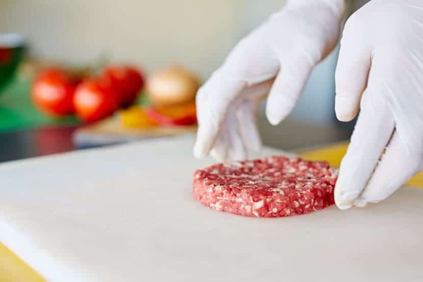 Einmalhandschuhe, die eine Hamburger-Patty in einer sauberen und hygienischen Küche zubereiten