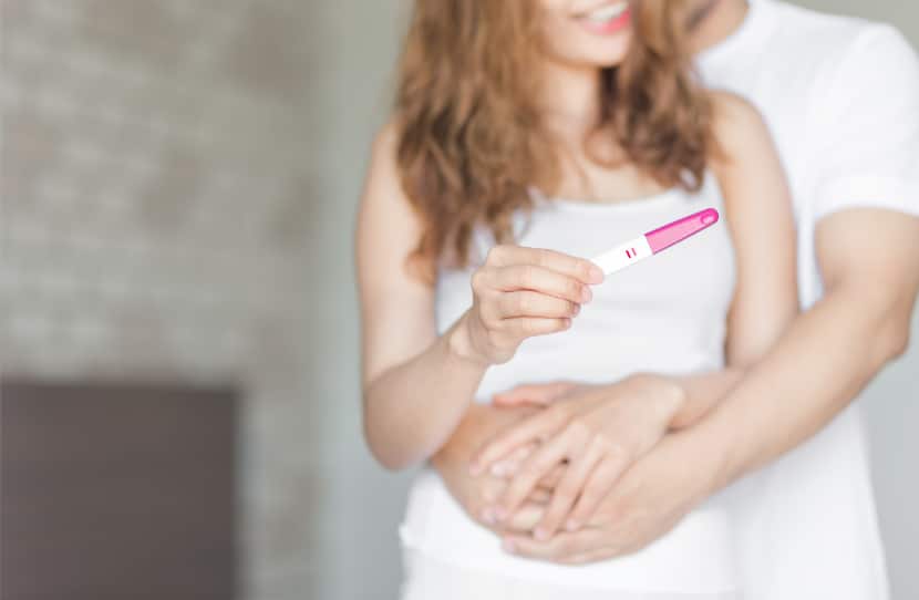 Glückliches Paar umarmt sich mit positivem Schwangerschaftstest in der Hand