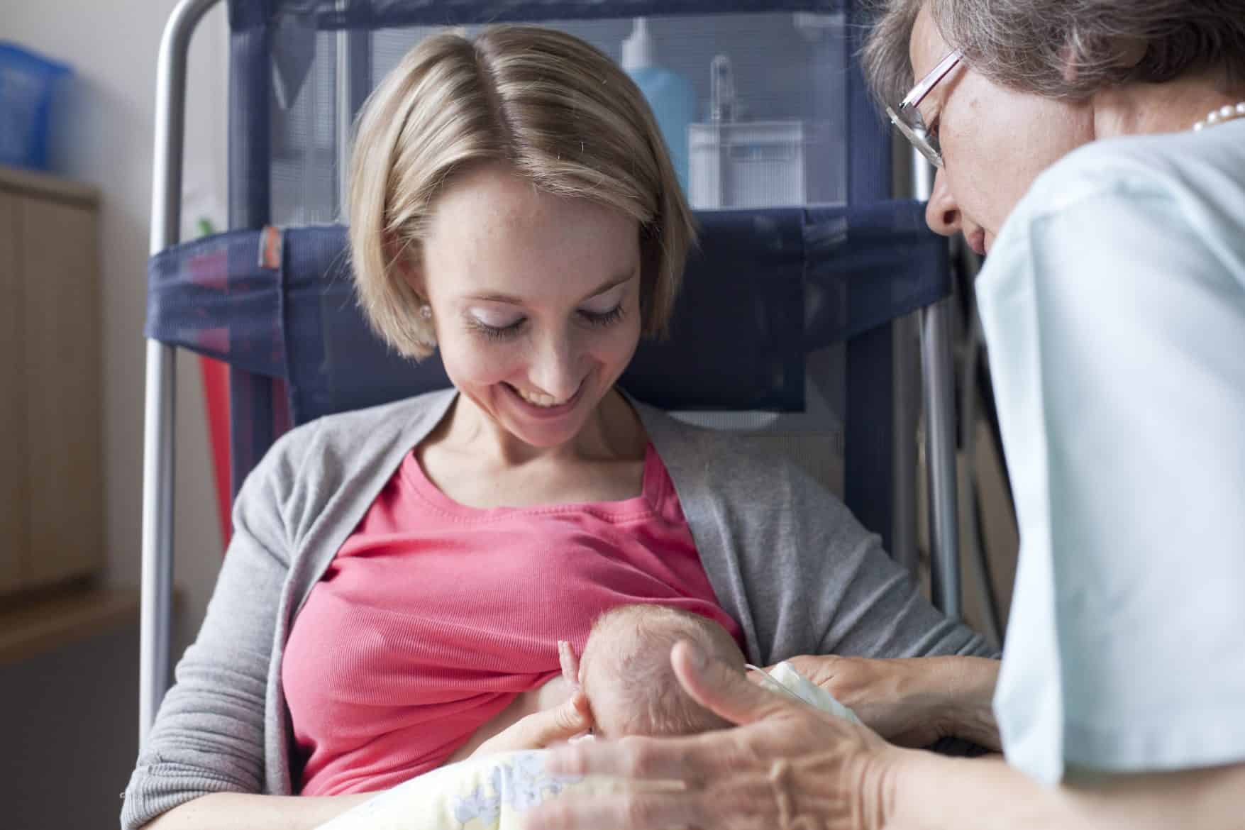 Eine Frau hält ein frühgeborenes Baby im Arm und stillt es, während eine Krankenschwester zusieht.