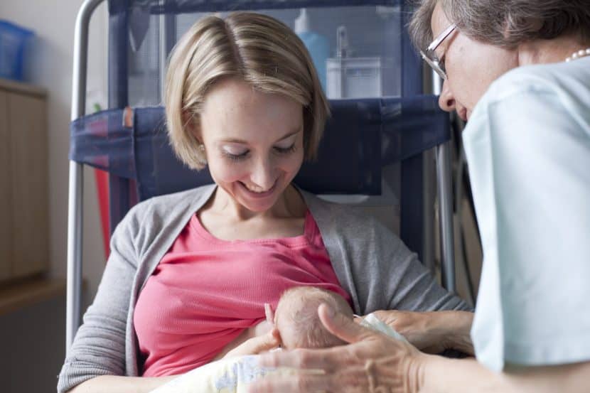 Eine Frau hält ein frühgeborenes Baby im Arm und stillt es, während eine Krankenschwester zusieht.