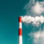 Rauchender Kaminschlot einer Fabrik vor blauem Himmel