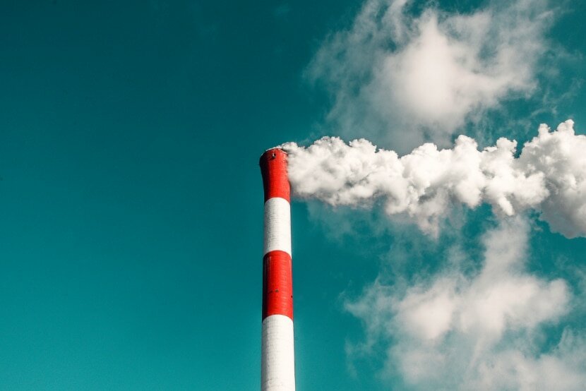 Rauchender Kaminschlot einer Fabrik vor blauem Himmel