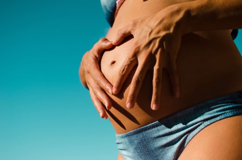 Babybauch, Schwangere im Bikini faltet Hände in Herzform